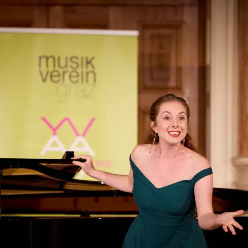 A singer in a green dress stands in front of a piano, smiling. | © Kurt Remling
