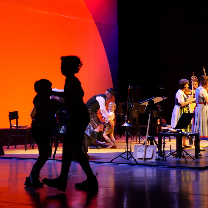 Persone danzanti in siluetta mentre una band si esibisce sul palco. | © Styriarte - ct