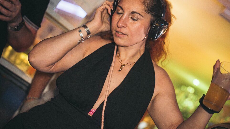 Una donna in un outfit nero con cuffie balla tenendo un drink. | © SilentDiscoAustria_Anuar Nakyssov