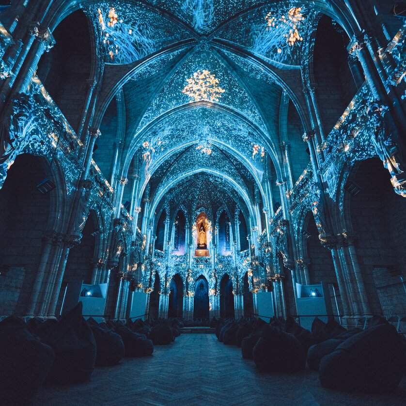 Beleuchtete, verzierte Kathedrale mit Sitzkissen im Vordergrund. | © Projektil