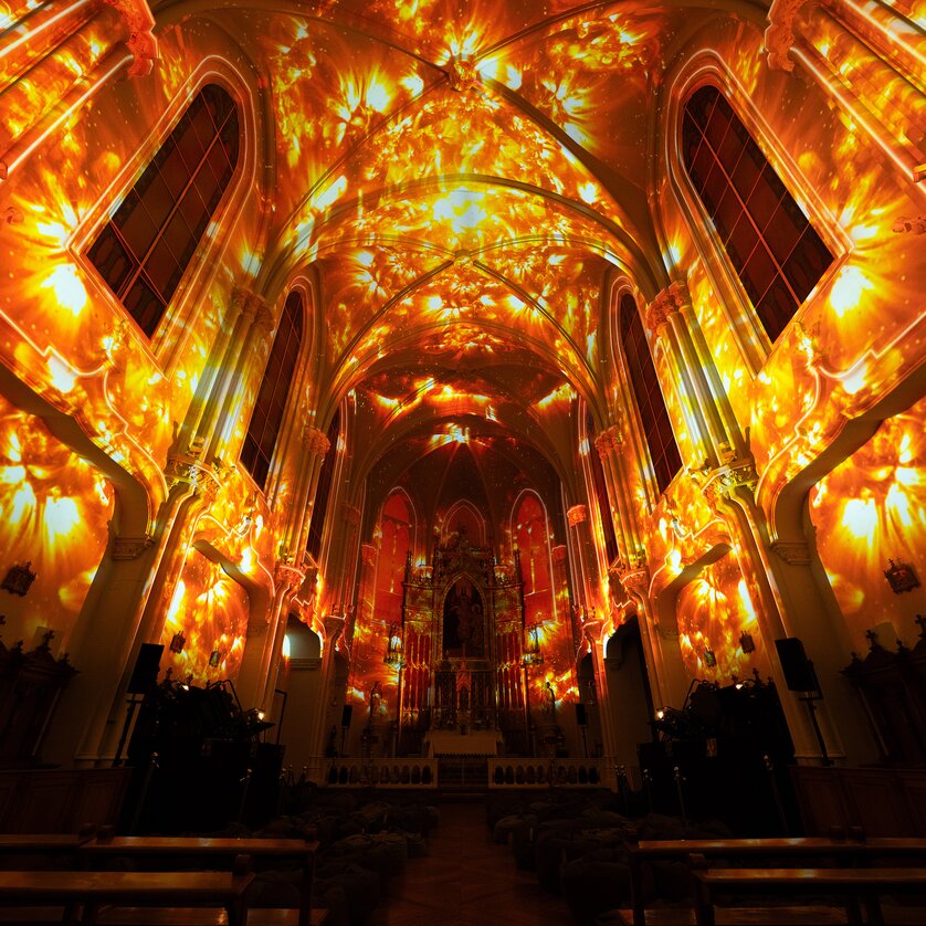 Ein Kircheninneres, lebhaft erleuchtet von warmen Lichtmustern. | © Projektil