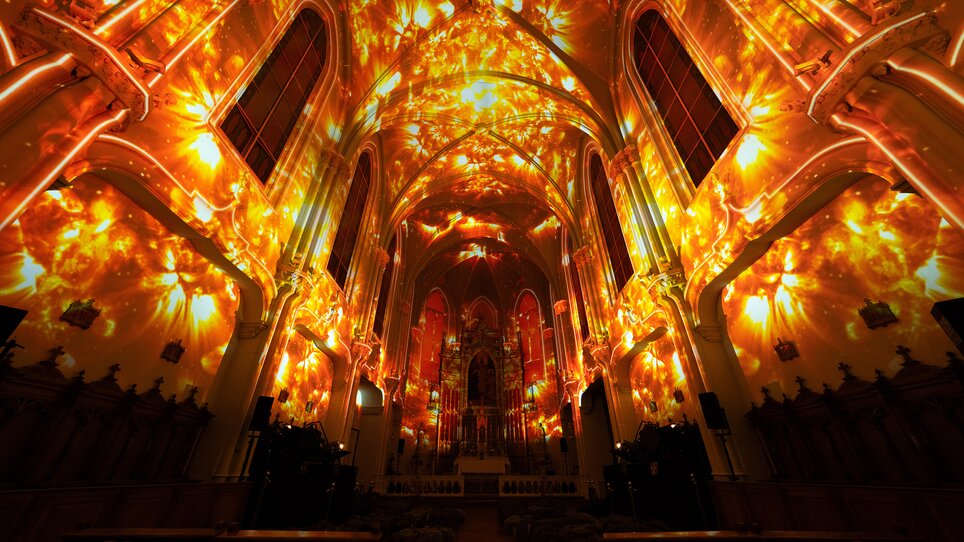 Ein Kircheninneres, lebhaft erleuchtet von warmen Lichtmustern. | © Projektil