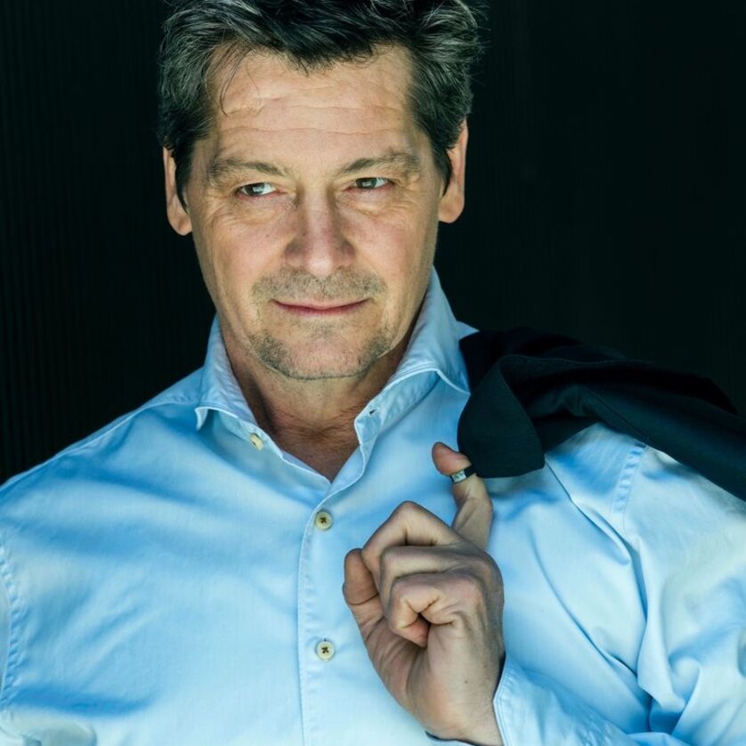 Ein Mann in einem blauen Hemd mit Jacke lächelt nachdenklich. | © Dorothee Falke