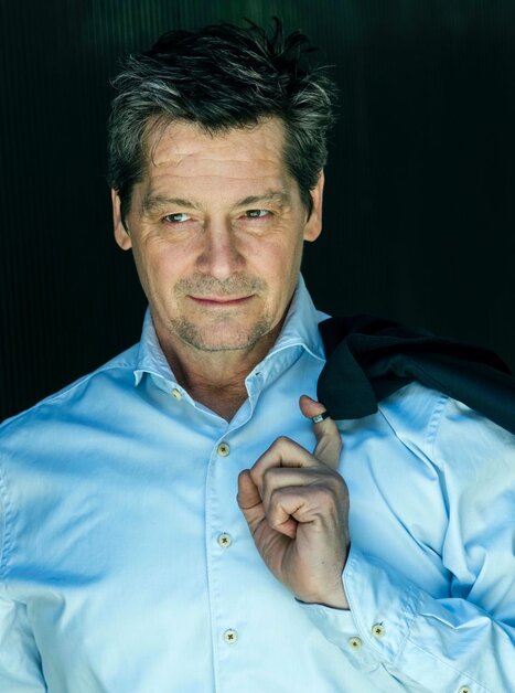 Ein Mann in einem blauen Hemd mit Jacke lächelt nachdenklich. | © Dorothee Falke