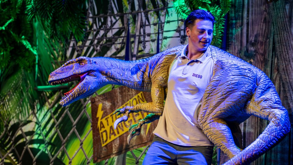 A young man is posing with a dinosaur puppet on stage at a dinosaur show. | © Timo Tutschek