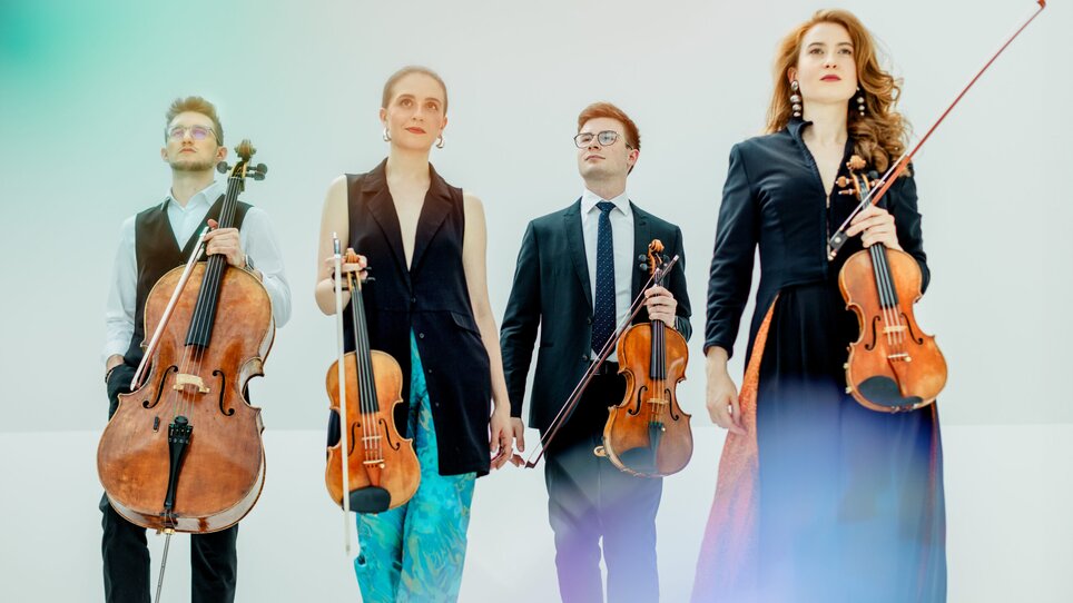 Four musicians with violins and a cello pose in elegant attire. | © Theresa Pewal