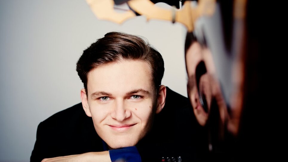 Ritratto di Dominik Wagner con un sorriso, appoggiato al pianoforte. | © Julia Wesely