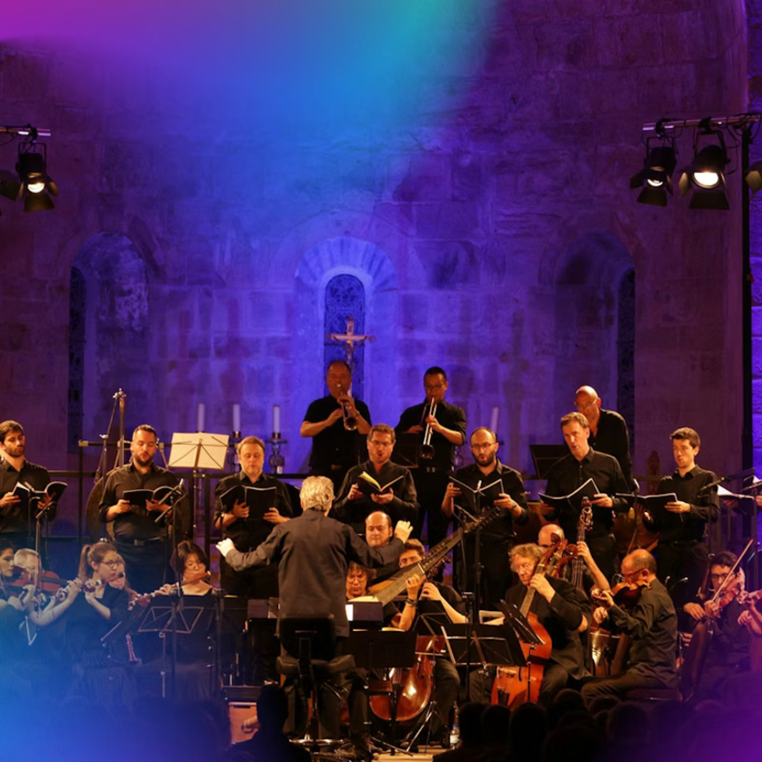 An orchestra performs under a conductor in an illuminated church. | © pouyfourcat