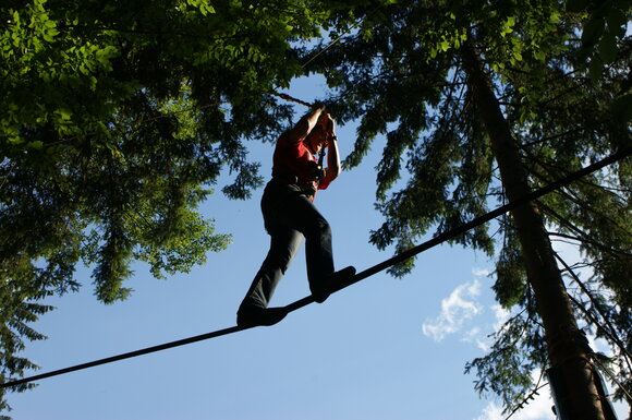 Person balancing on a rope between trees under a blue sky.