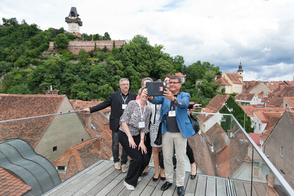Group of five people posing on a rooftop terrace with a view of Graz and the clock tower.