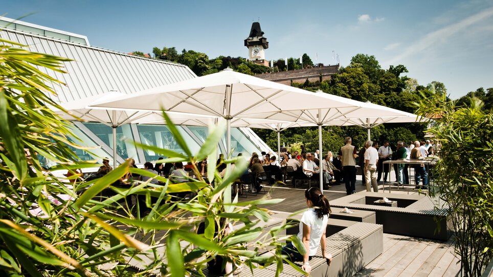 Dachterrasse mit Gästen, Blick auf den Grazer Uhrturm und die Stadt Graz.
