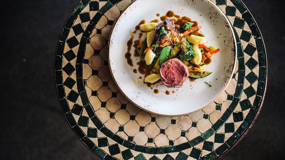 A delicate dish featuring meat and vegetables on an artistic table. | © Aiola im Schloss