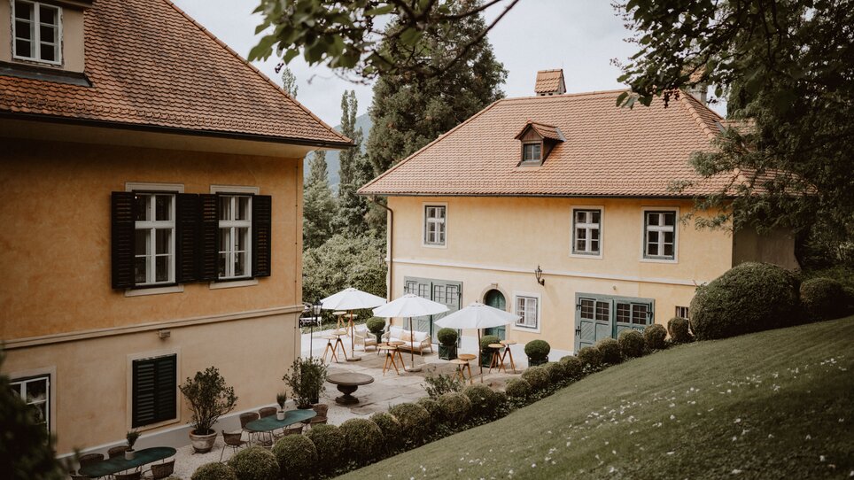 Two yellow buildings surrounded by greenery with outdoor umbrellas. | © Stefan Mang Photography