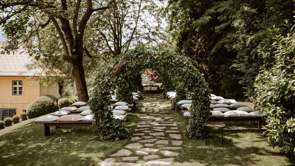 Idyllic garden with cushioned benches and an arch of plants. | © Stefan Mang Photography