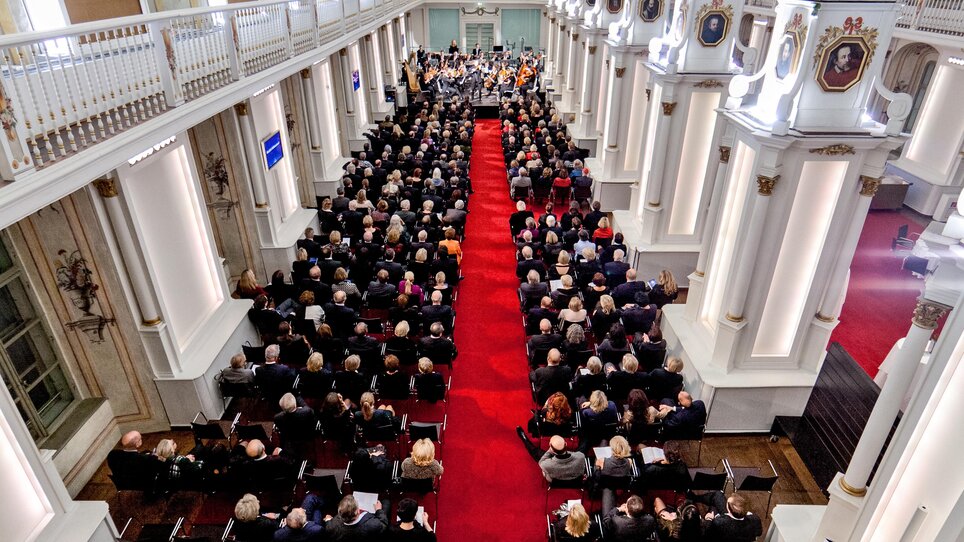 Participants in formal attire gather in the Old University hall for a conference. | © Alte Universität