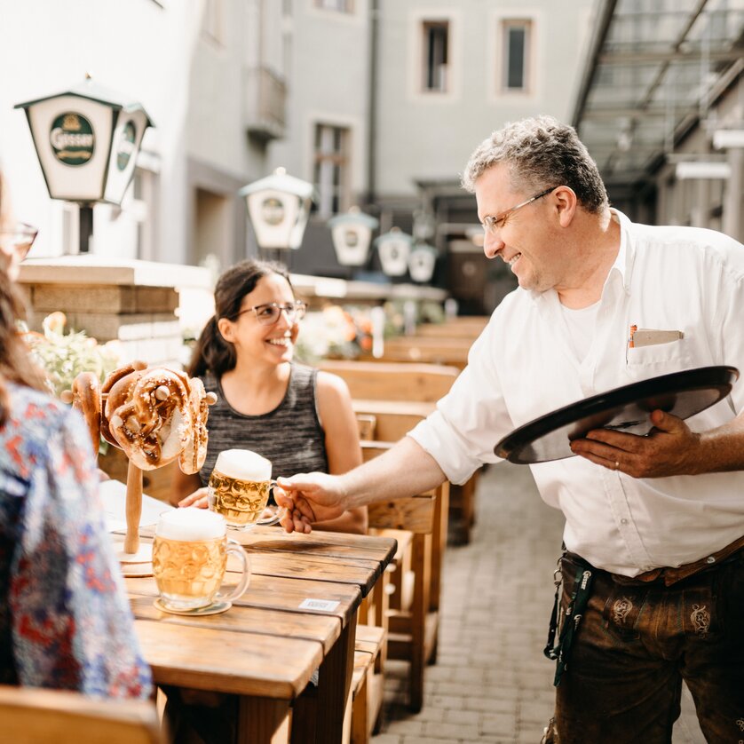 Un cameriere serve birra e brezel ai clienti nel giardino del ristorante Gösserbräu. | © glddggrs-35