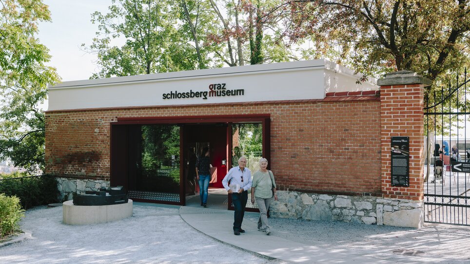 Two people walking towards Graz Schlossberg Museum, surrounded by trees. | © Sebastian Reiser