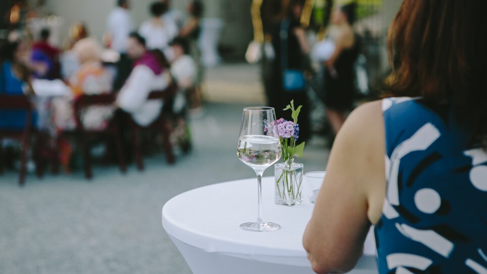 A person with a glass of water and flowers at an outdoor event. | © -Sebastian-Reiser