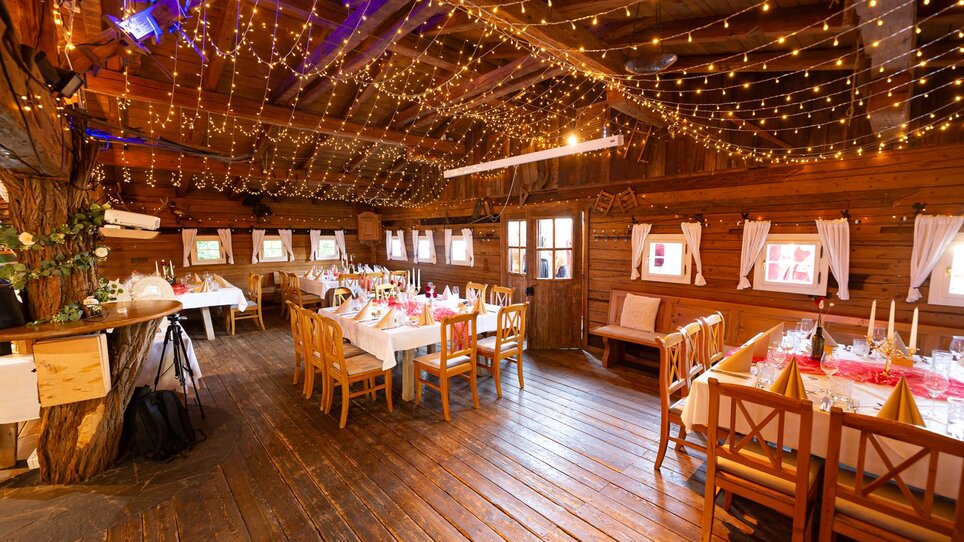 Innensicht der Almhütte Graz mit festlich gedeckten Tischen und Lichterketten. | © I AM Hotels