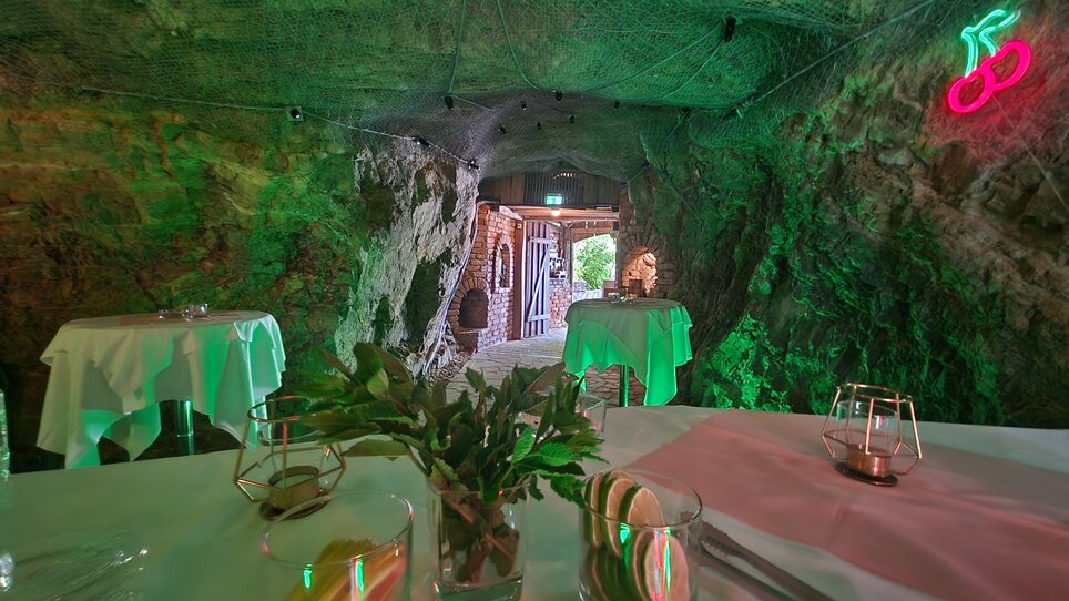 Innenansicht der Berggrotte neben der Almhütte Graz mit Tischen und natürlichem Stein. | © I AM Hotels