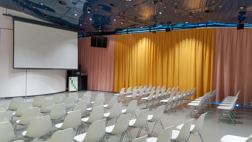 White-seated event space in Kunsthaus with screen. | © UMJ - N. Lackner