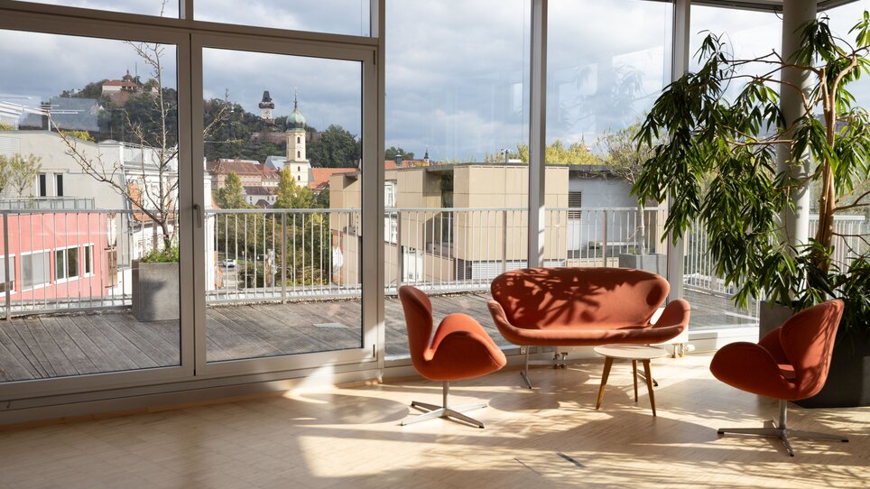 Die Level 4 Eventlocation bietet helle, moderne Räumlichkeiten mit Panoramafenstern, eleganten Möbeln und Blick auf den Grazer Uhrturm, ideal für Business-Events. | © Level 4