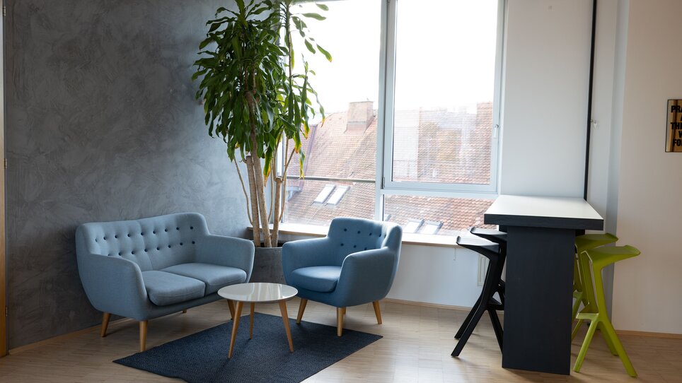 Gemütliche Lounge im Level 4 mit blauen Sofas, einem Tisch und Pflanzen. Helle, moderne Architektur bietet eine einladende Atmosphäre. | © Level 4