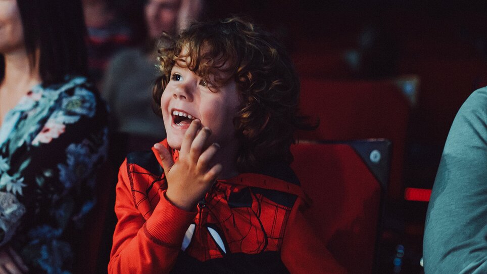 A child in a Spiderman outfit smiles joyfully during an event at Next Liberty. The stage is well-lit, creating a friendly atmosphere. | © Stella