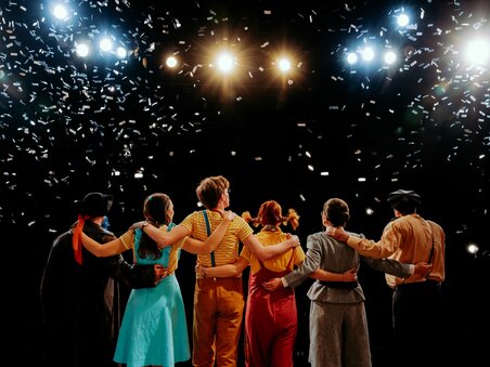 Il palcoscenico di Next Liberty presenta un gruppo di performer durante l'applauso finale. I coriandoli cadono e le luci del palco creano un'atmosfera festosa. | © Stella Kager