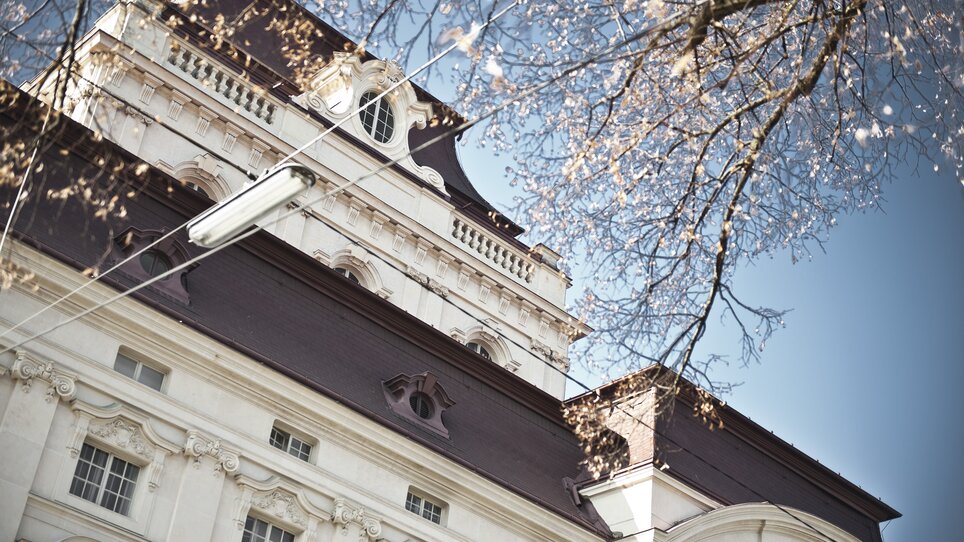 Upper façade of Graz Opera House with blossoming branches and blue sky | © Oper Graz