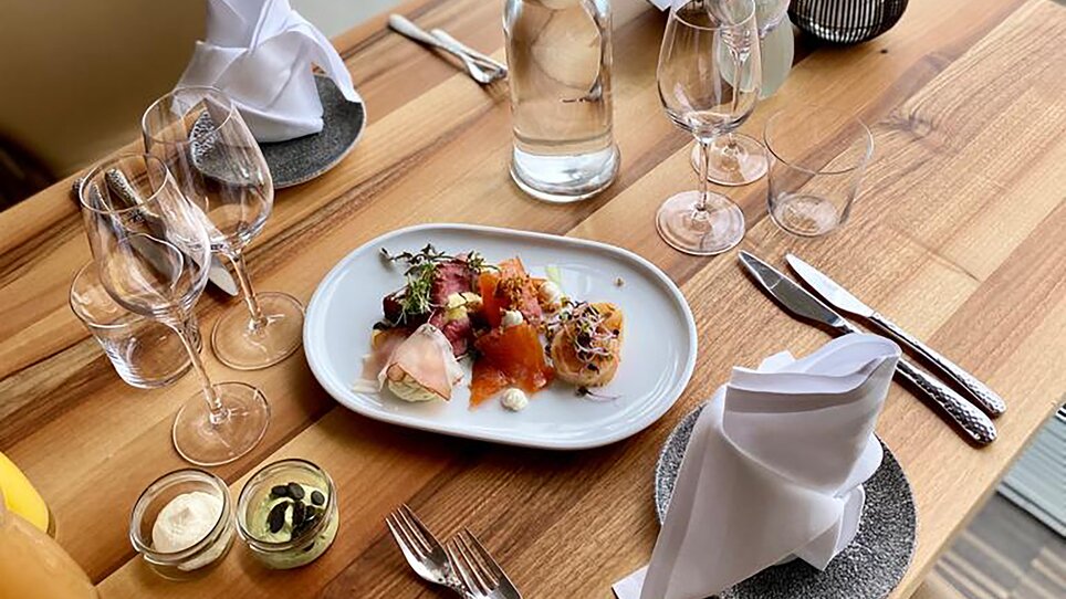 Im Restaurant SCHLOSSBERG sind ein gedeckter Tisch, edles Geschirr und moderne Architektur zu sehen. Der Raum bietet eine stilvolle Atmosphäre und eignet sich für geschäftliche Veranstaltungen. | © Restaurant SCHLOSSBERG