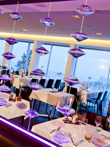 Moderne Innenausstattung mit Tischanordnung, großen Fenstern und Beleuchtung im Schlossberg Restaurant. Ideal für Konferenzen und Geschäftsmeetings. | © Schlossberg Restaurant