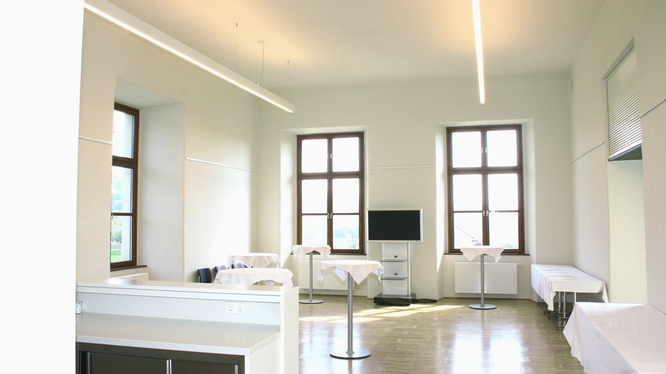 Ein heller, moderner Raum in Stift Rein mit Tischen, Fenster und einem TV. Ideal für Konferenzen und Meetings.