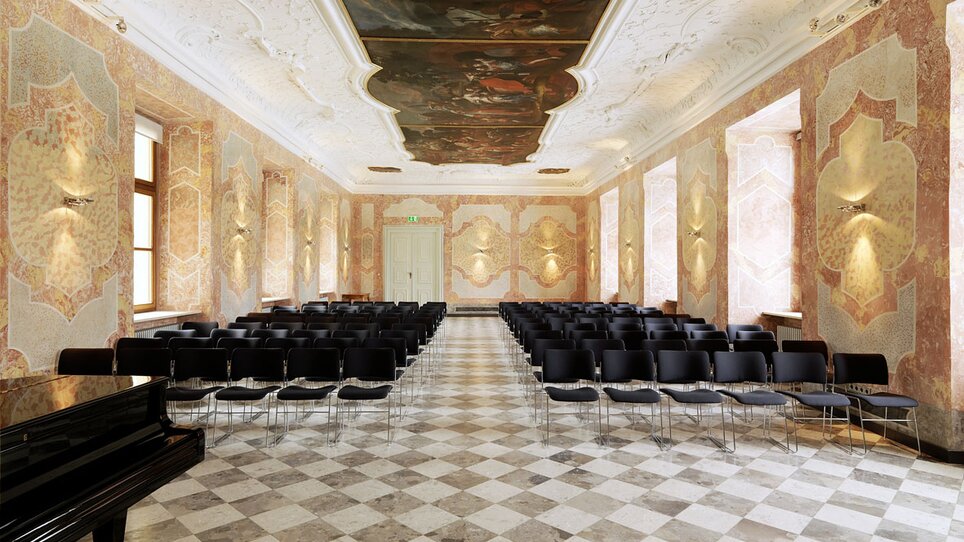 Eleganter Raum im Stift Rein bietet Platz für Veranstaltungen. Hohe Decken, stilvolle Möbel und ein Klavier schaffen eine einladende Atmosphäre.