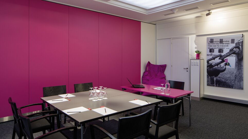 Ein moderner Konferenzraum mit pinken Wänden, Tisch und Medienausstattung. | © Austria Trend Hotel Europa Graz