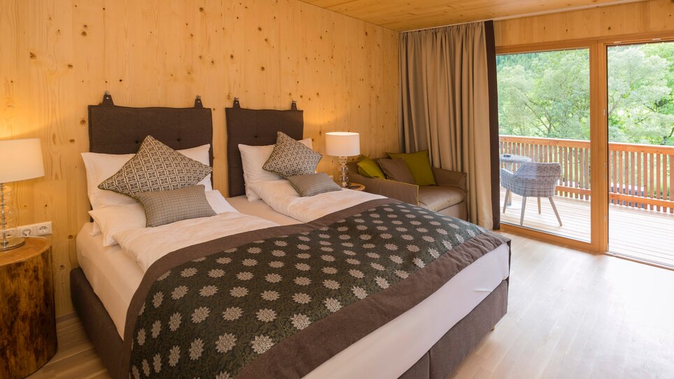 Ein modernes Hotelzimmer mit Holzvertäfelung, zwei Betten und einem Balkon in der Genusspension Herti. | © Grossauer