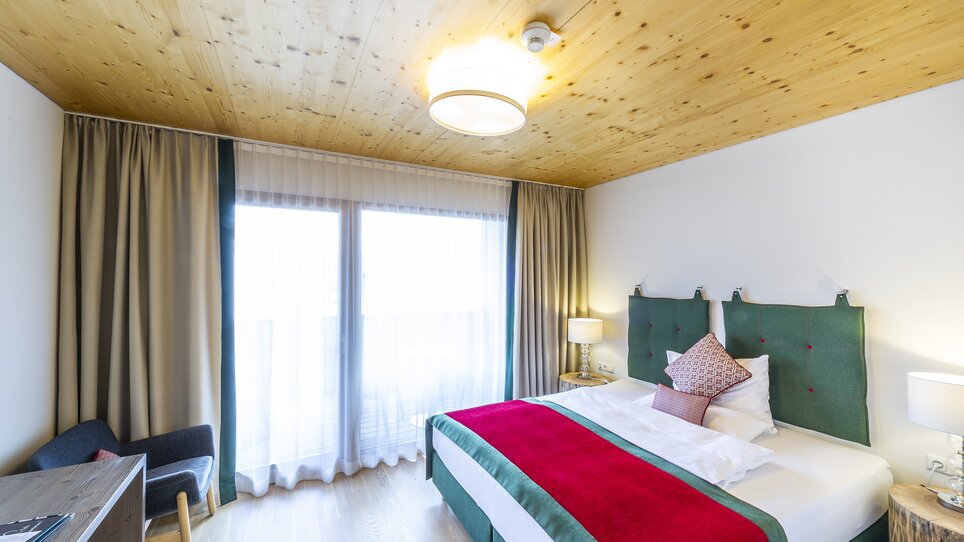 Modernes Zimmer mit Doppelbett, einem gemütlichen Sessel und viel Licht in der Genusspension Herti. | © Grossauer
