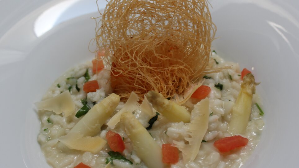 Ein feines Spargelrisotto mit frittiertem Teig auf einem weißen Teller serviert im Hügellandhof. | © Hügellandhof