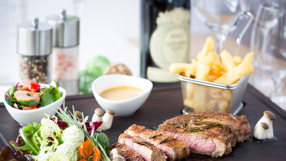 Ein saftiges Steak mit Salat, Pommes und Soße in eleganter Präsentation serviert im Hügellandhof. | © Hügellandhof