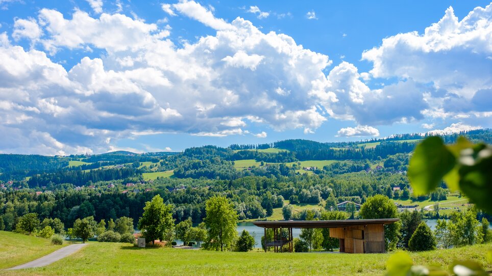 Weite Aussicht auf grüne Hügel und ein Gewässer bei blauem Himmel. | © iQ-Foto - Thomas Leibetseder