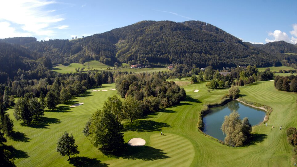 Panoramic view of a golf course surrounded by mountains and a pond close to Murhof Hotel & Restaurant. | © Murhof