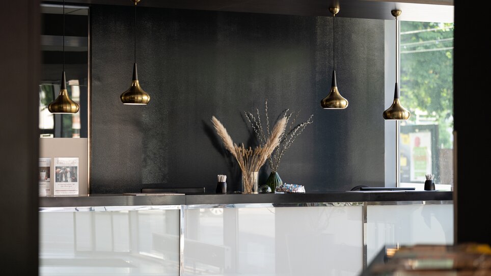 Ein eleganter Empfangsbereich mit goldenen Lampen und Pflanzendekoration im PLAZA INN Graz City. | © PLAZA INN Graz City