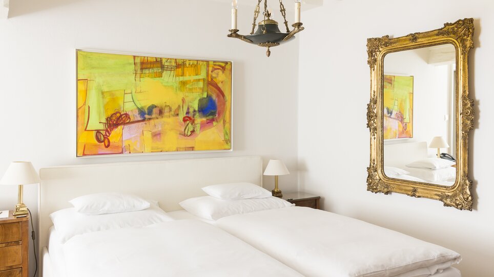 Bright bedroom with two beds, artwork, and mirror in Schlossberghotel. | © Schlossberghotel
