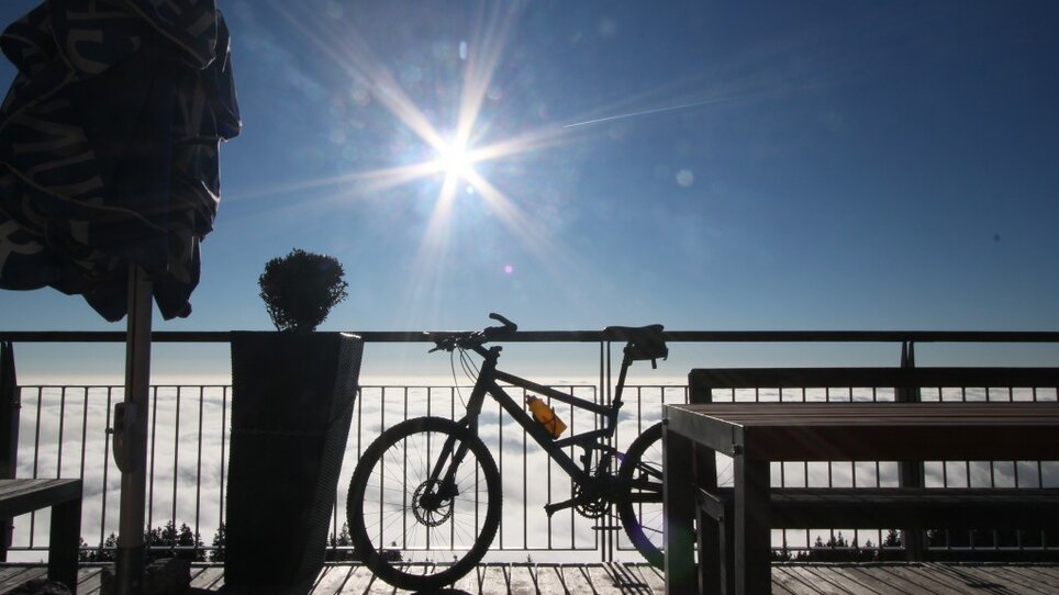 Fahrrad und Terrasse mit Blick über Wolken bei Sonnenlicht vorm Stubenberghaus. | © Stubenberghaus