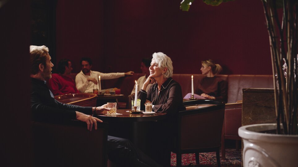 Zwei Personen bei einem Gespräch in einer stilvollen Lounge im Hotel Weitzer mit Kerzenlicht. | © Florian Weitzer Hotels & Restaurants
