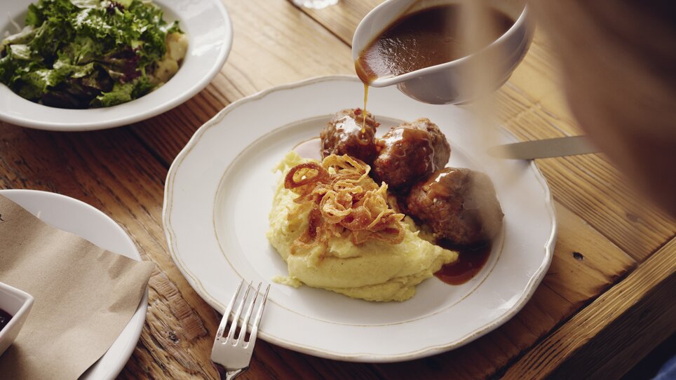 Fleischbällchen auf cremigem Püree mit Zwiebeln und Sauce, daneben ein Salat, kredenzt im Restaurant Der Steirer des Hotel Weitzer. | © Florian Weitzer Hotels & Restaurants