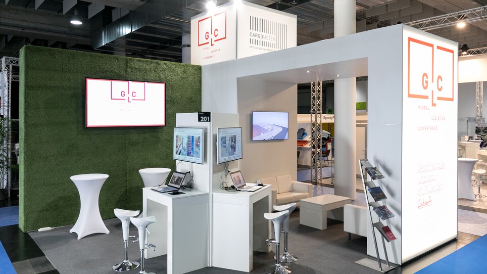 Moderne Messefläche mit Sitzgelegenheit und Präsentationstechnik, AMB. Ausstattung umfasst Tische, Stühle sowie digitale Bildschirme. | © AMB GmbH