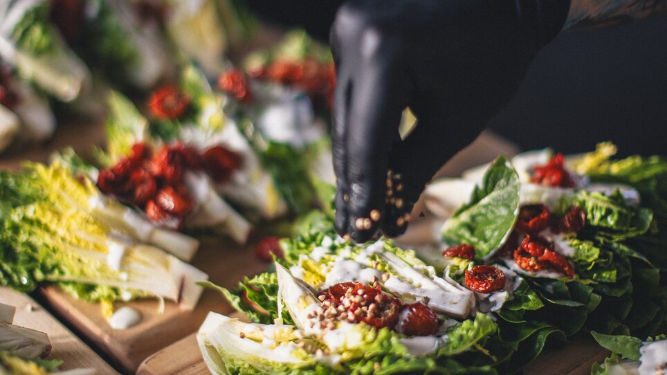 Von der Cateringfirma The Underground Kitchen werden frische Salatgerichte zubereitet. Ein Koch fügt Zutaten zu den Salaten hinzu, die geschmackvoll angerichtet sind. | © Alex Rauch