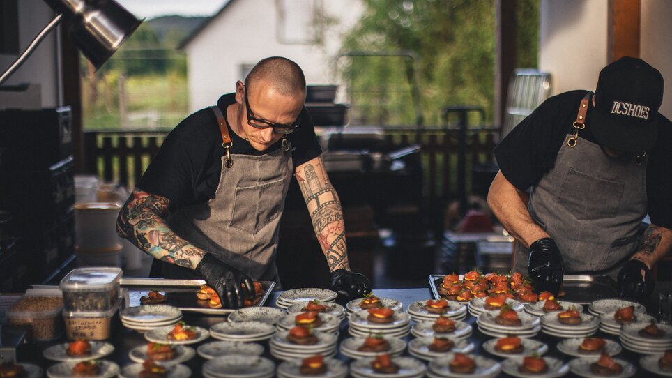 Zwei Köche von The Underground Kitchen // bereiten kunstvolle Häppchen in einer lichtdurchfluteten Küche vor. Fokus auf High-End-Tellerpräsentation und professioneller Atmosphäre. | © Alex Rauch