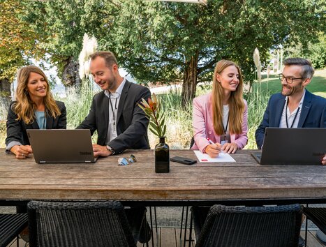 Vier Personen arbeiten an Laptops bei einem Geschäftstreffen im Freien. | © Graz Tourismus - Mias Photoart